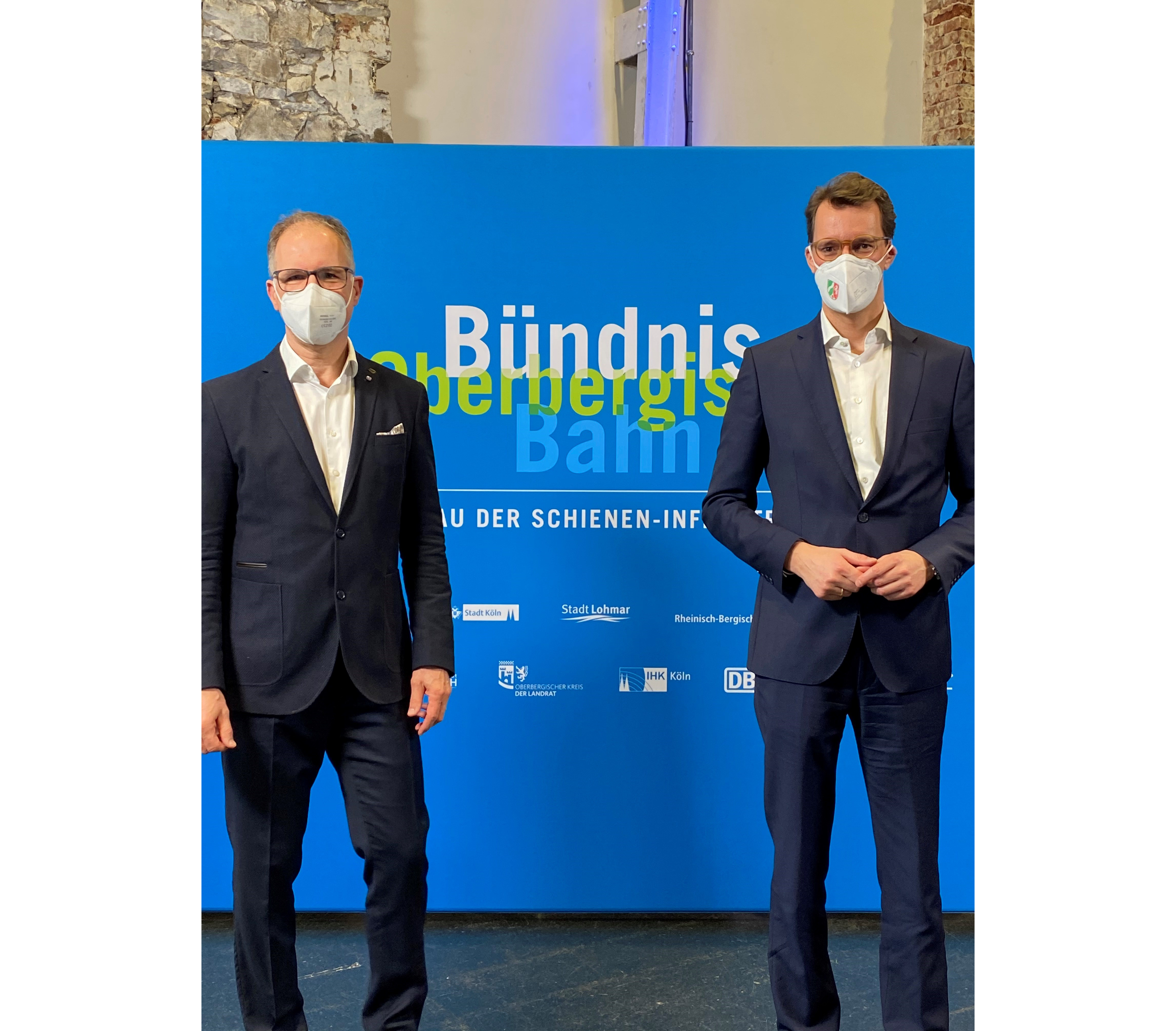 Dr. Norbert Reinkober und Hendrik Wüst stehen einträchtig nebeneinander. Im Hintergrund steht ein Plakat, das die Partner des Bündnisses Oberbergische Bahn zeigt.