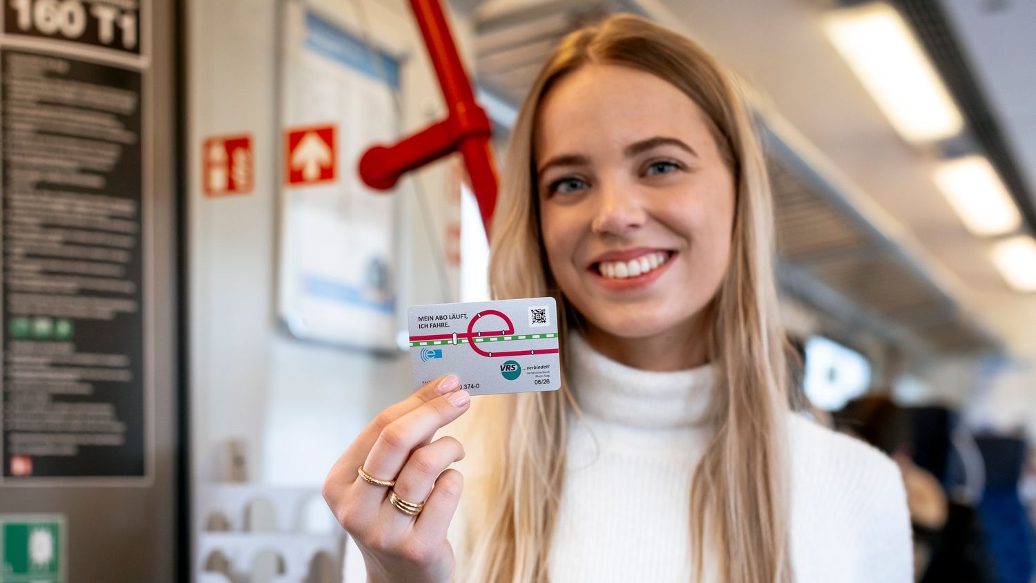 Ein Bild zeigt eine Kundin in einer S-Bahn, die lächelnd ihr Deutschlandticket präsentiert.