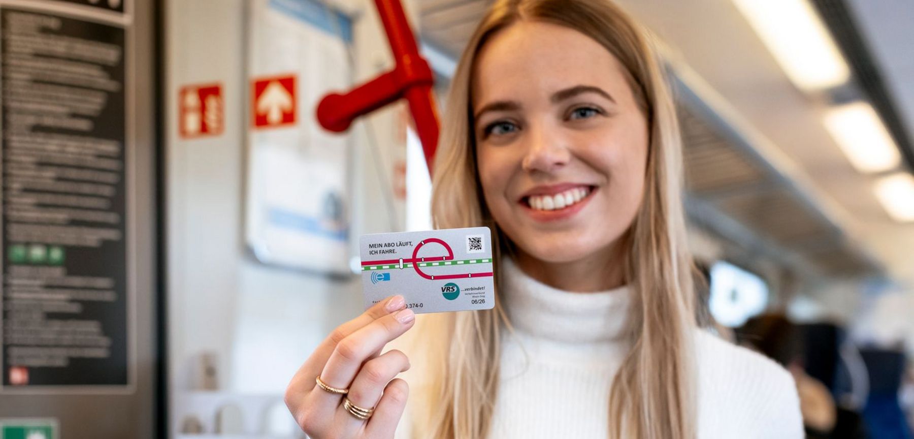 Ein Bild zeigt eine Kundin in einer S-Bahn, die lächelnd ihr Deutschlandticket präsentiert.