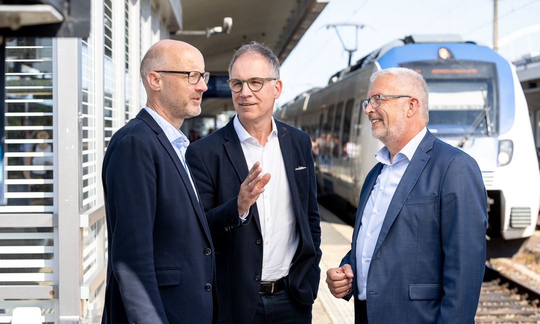 Wir sehen, wie Jens Schäfer, Norbert Reinkober und Manfred Gutfrucht zusammen auf einem Bahnsteig stehend miteinander sprechen.