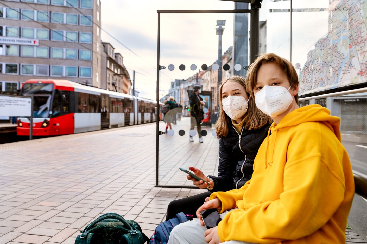 Zwei junge Frauen mit Masken warten auf ihren Zug und sind trotz der Pandemie-bedingten Einschränkungen gut gelaunt.
