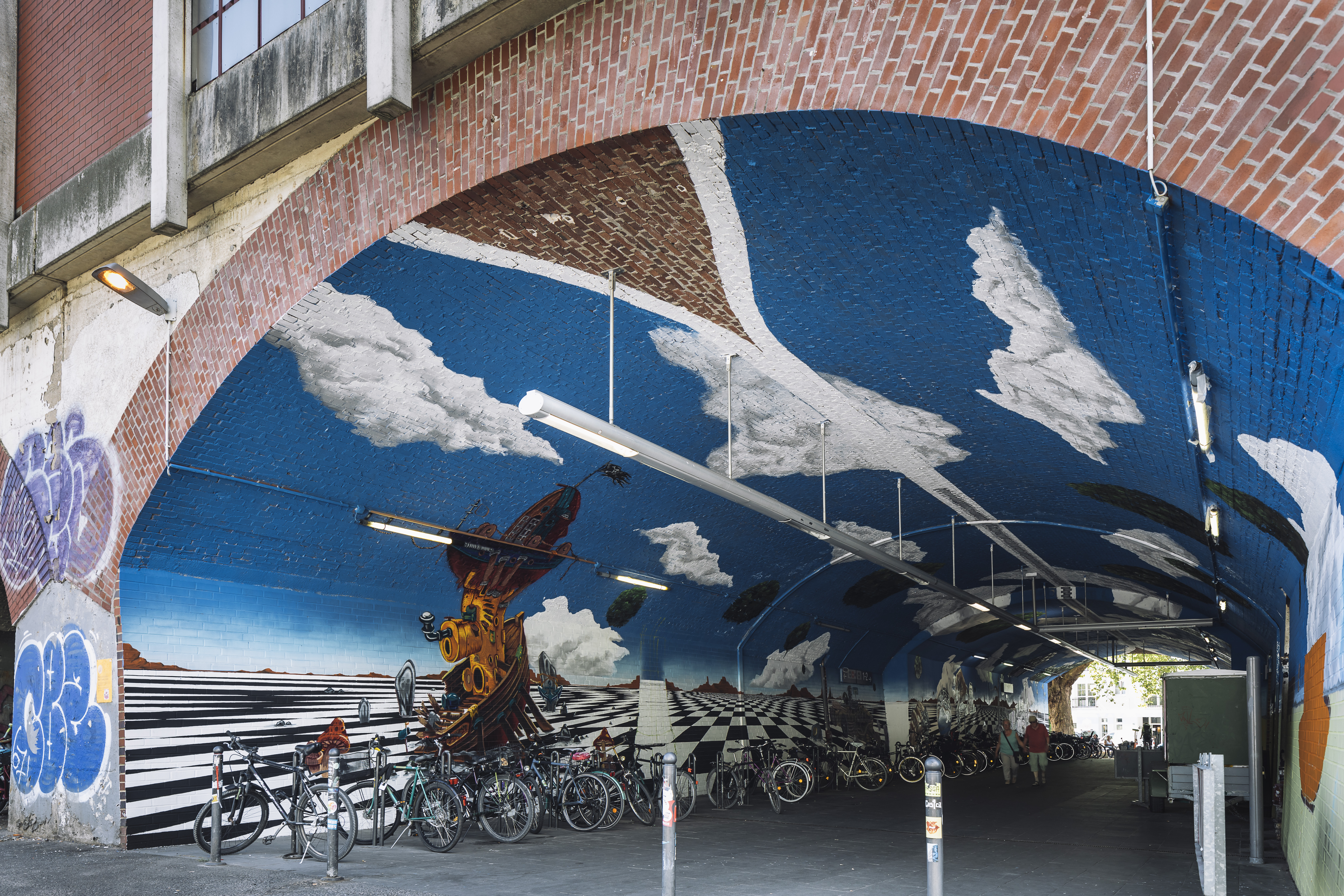 Ein Bild zeigt ein großangelegtes Graffiti im Gewölbegang einer Station. Darauf zu sehen sind Wolken auf einem strahlend blauen Himmel.