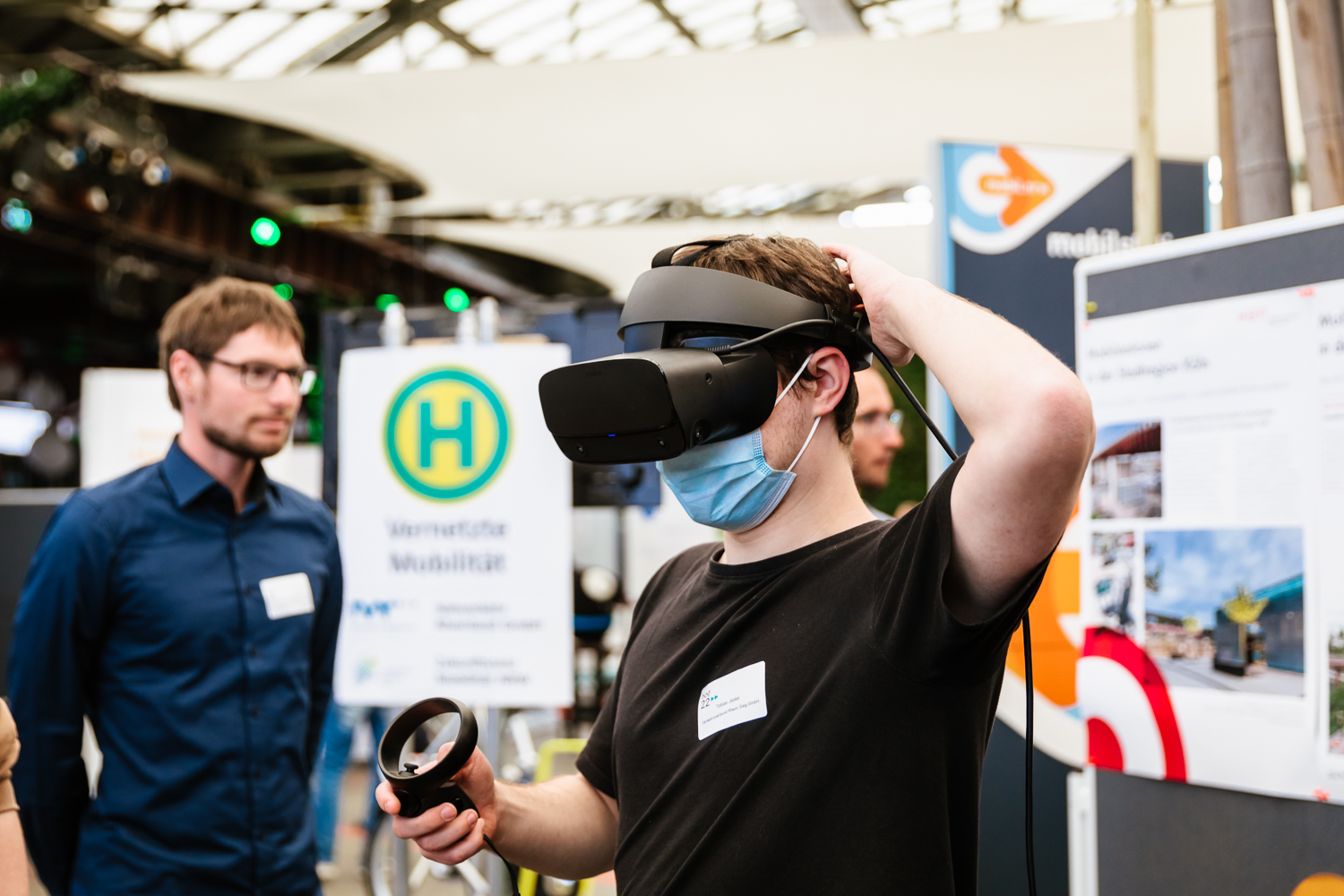 Wir sehen einen Besucher der Mobilitätsakademie, der mit einer Virtual Reality-Brille eine Mobilstation digital erkundet.