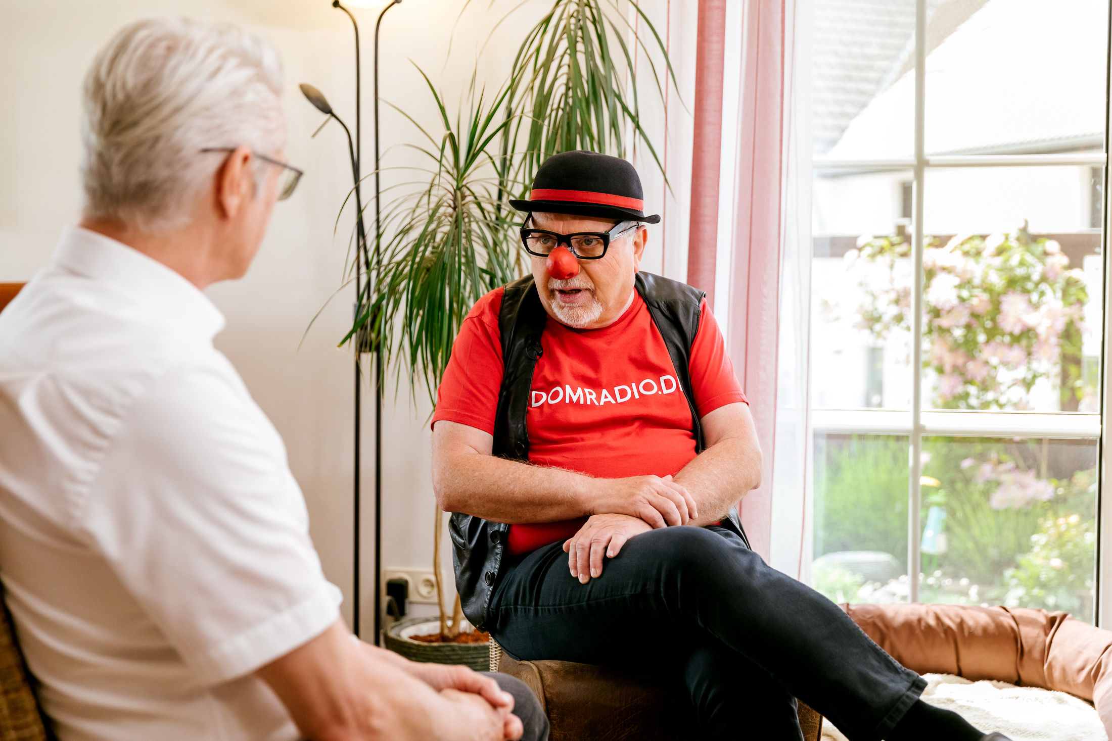 Ein Bild zeigt Willibert Pauels, wie er mit Pappnase und Hut mit Michael Vogel spricht.